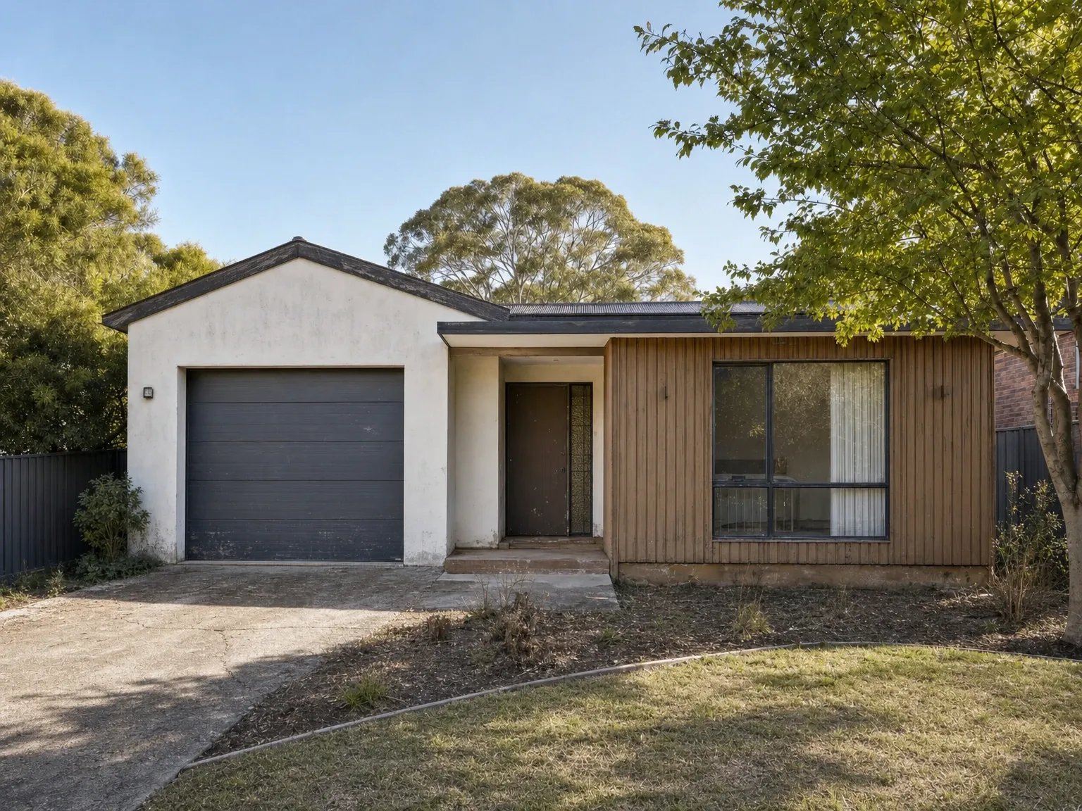 Tired Australian suburban house facade with dated cladding and an overgrown front garden