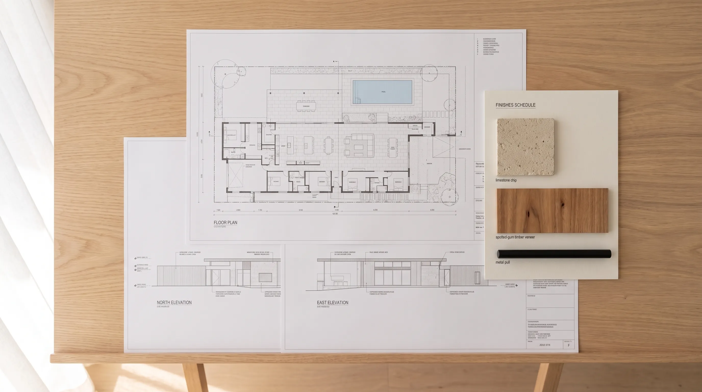 Styled flat-lay of the interior study documents: floor plan, elevations and finishes schedule with material samples