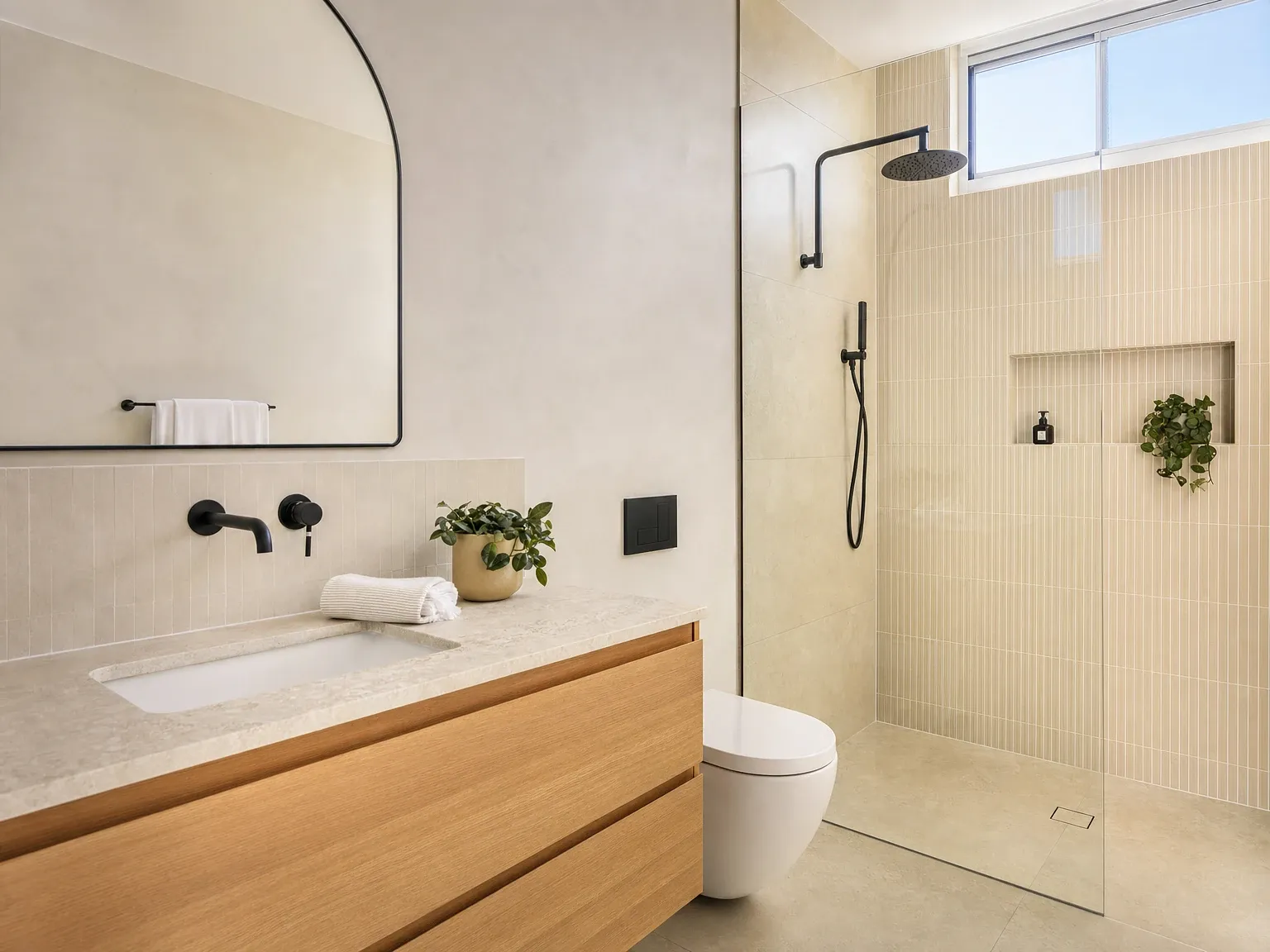 The same bathroom after a warm modern renovation with stone-look tiles, timber vanity and matte black tapware