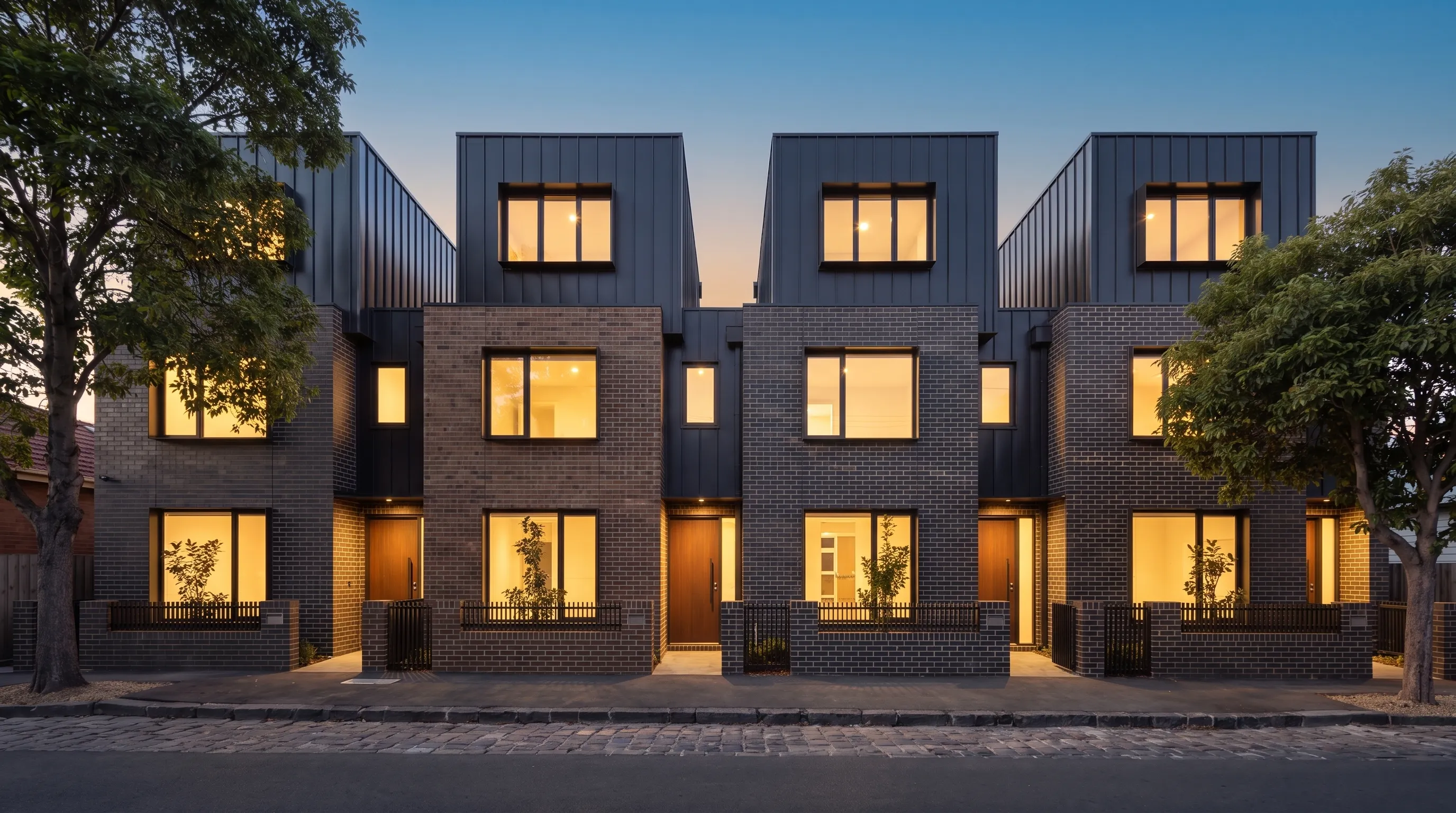 Townhouse study: row of four Melbourne townhouses at dusk, lit windows in face brick and standing-seam facades