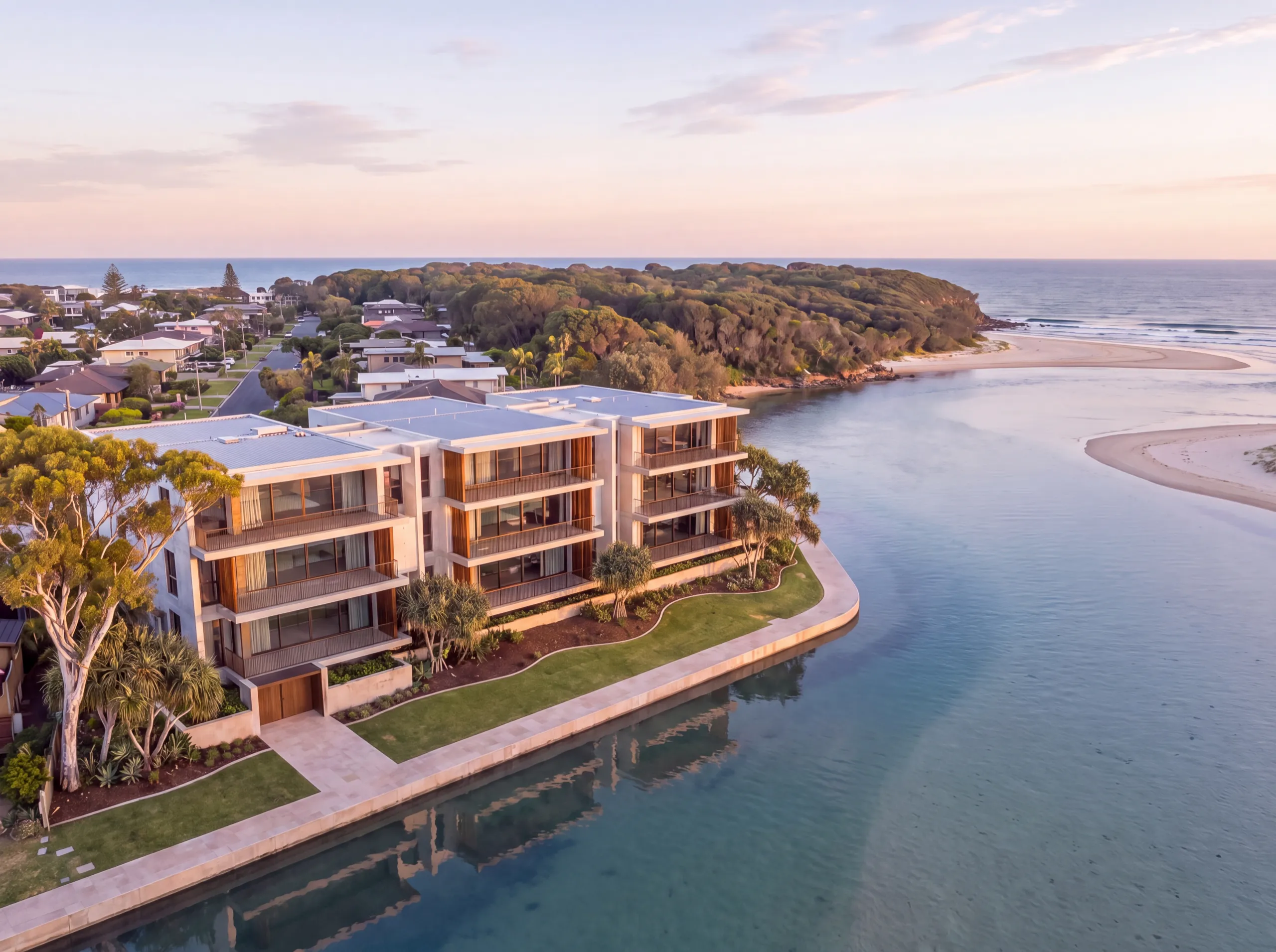 Late-afternoon aerial of the project on the creek mouth, with the sand spit, bushland headland and surf beach beyond